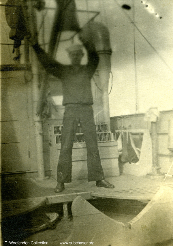 Crewman with flags standing on bridge wing near wherry support.